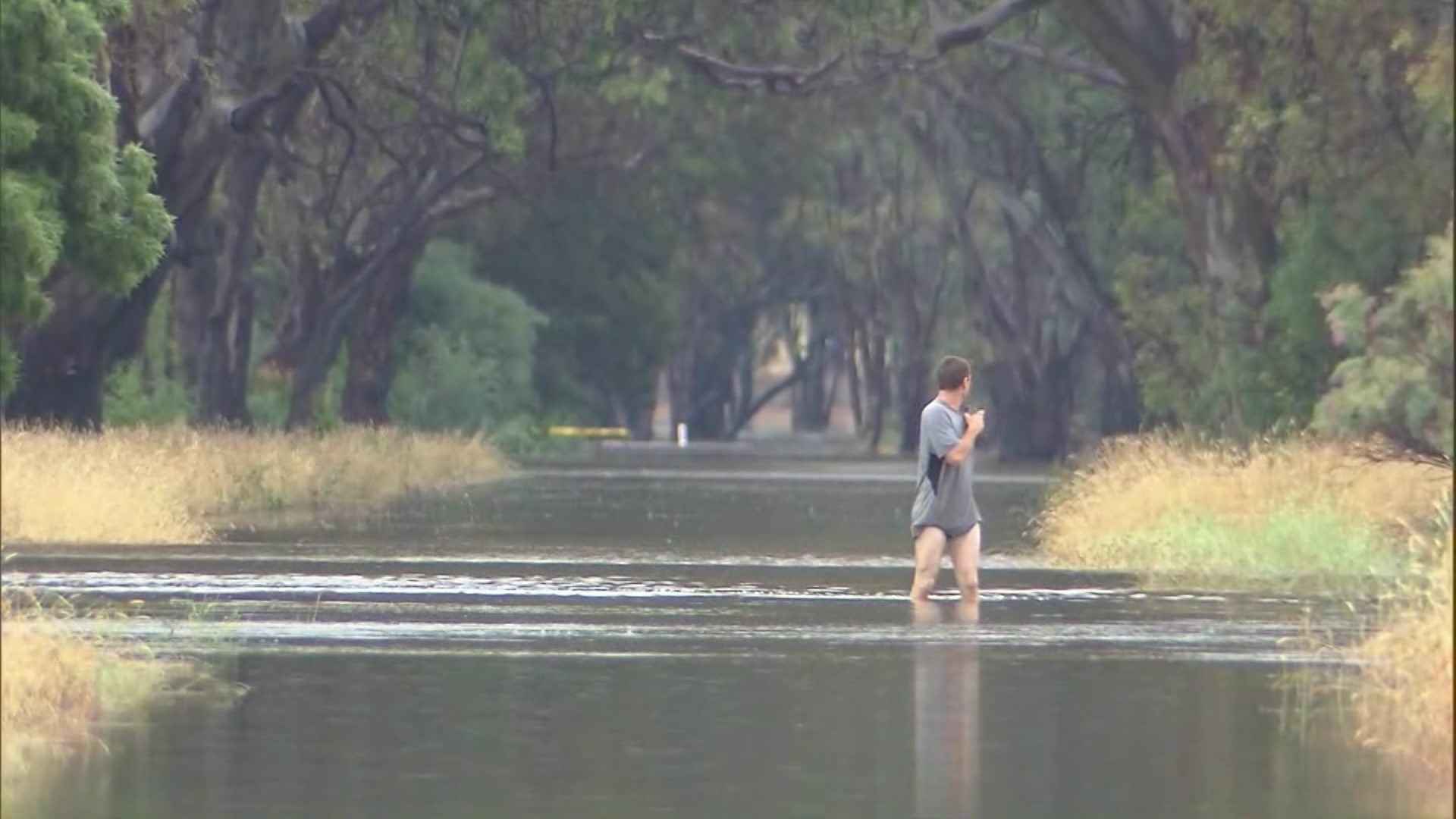 A man standing in knee deep water on a road. 