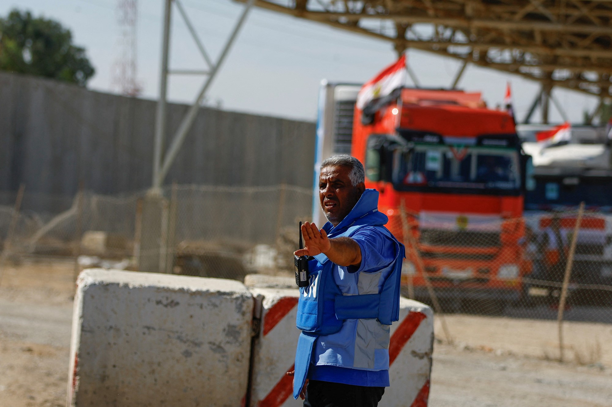 A UN worker in a blue vest gestures in front of an orange truck.