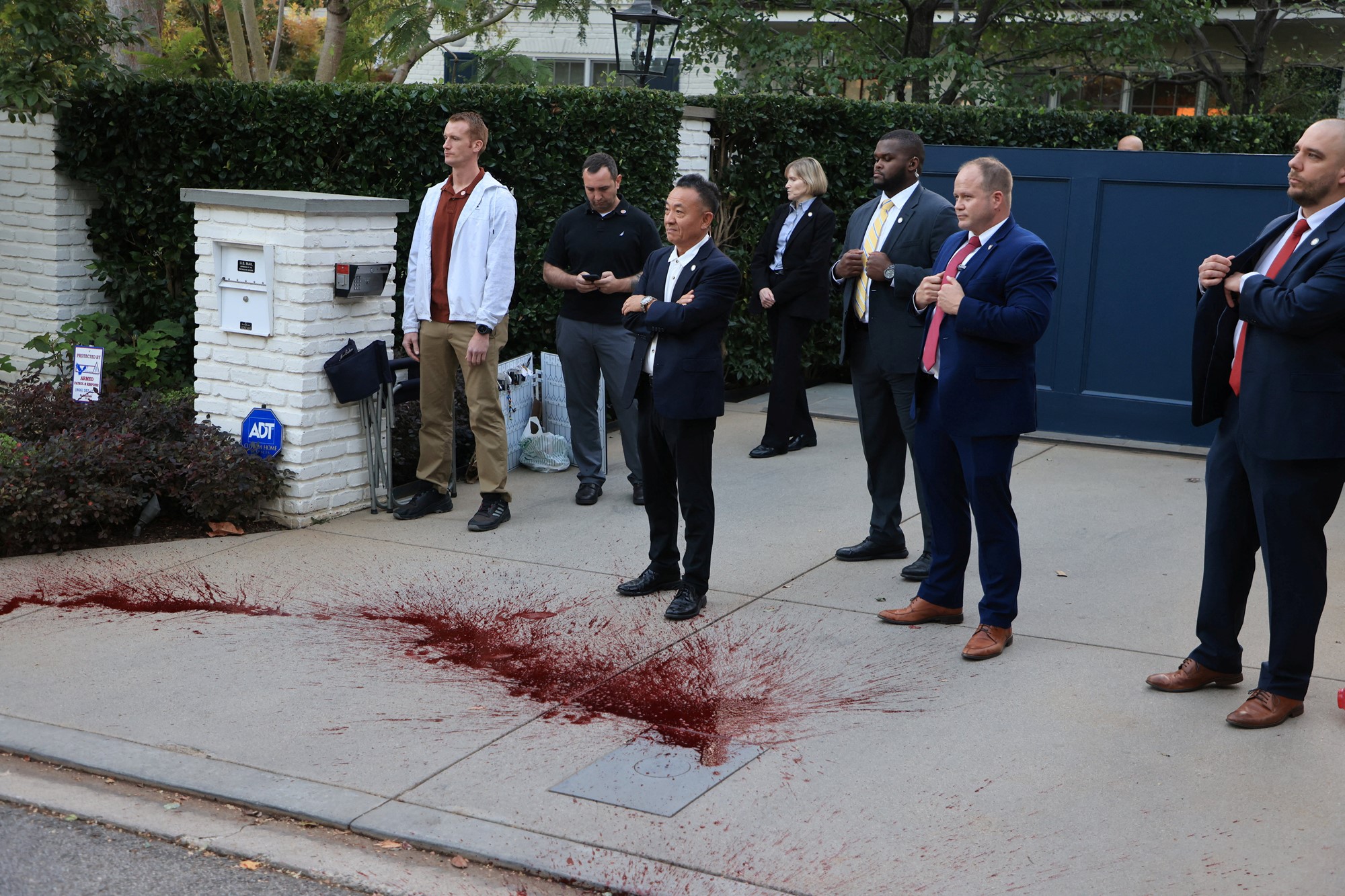 People stand with arms crossed looking in front spilt fake blood on a driveway