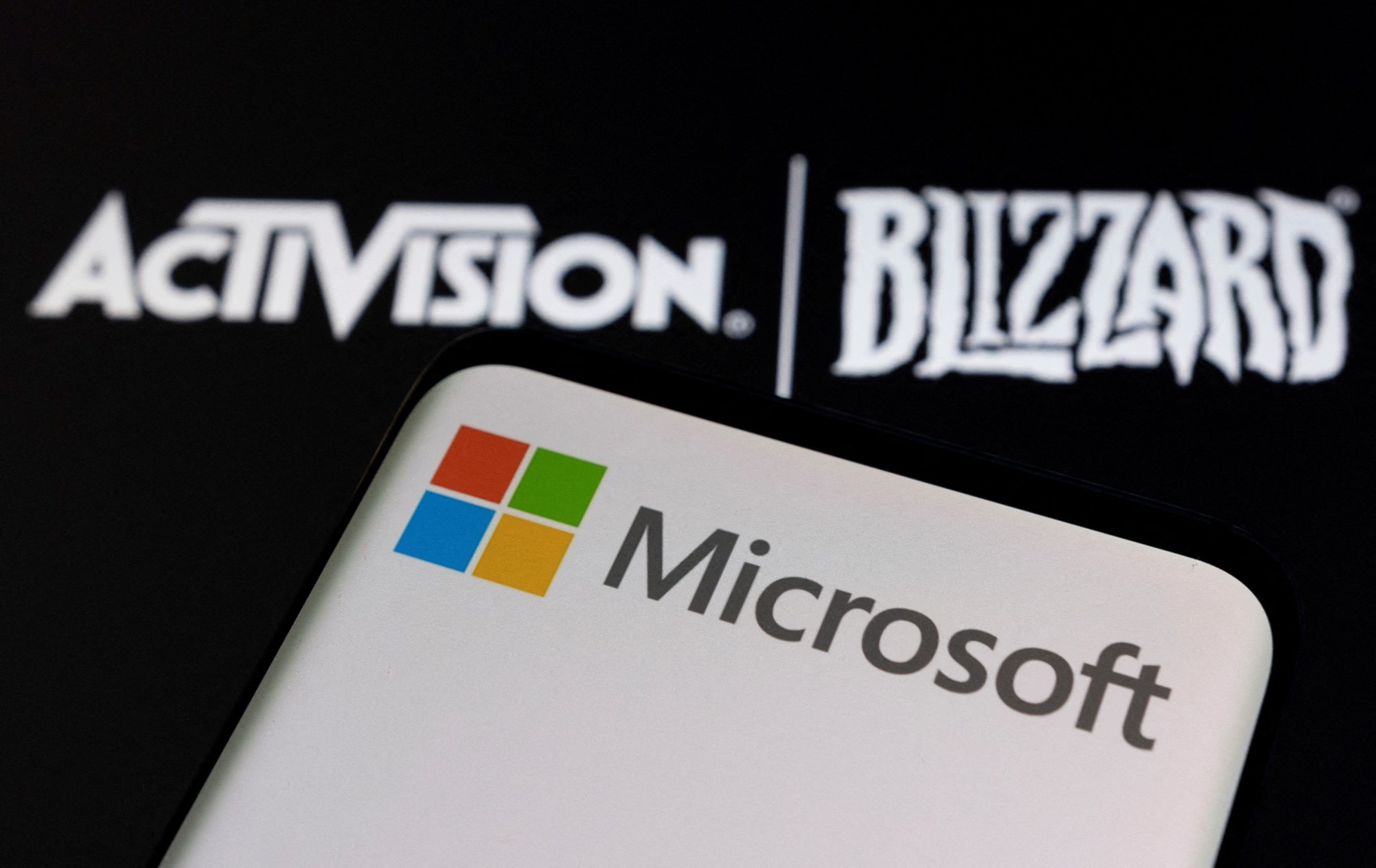 A phone displaying the Microsoft logo, in front of the Activision and Blizzard logos behind