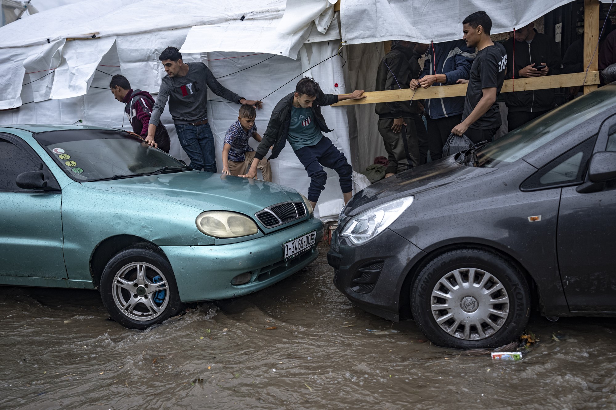 Children balance as they walk across rainwater between two cars 