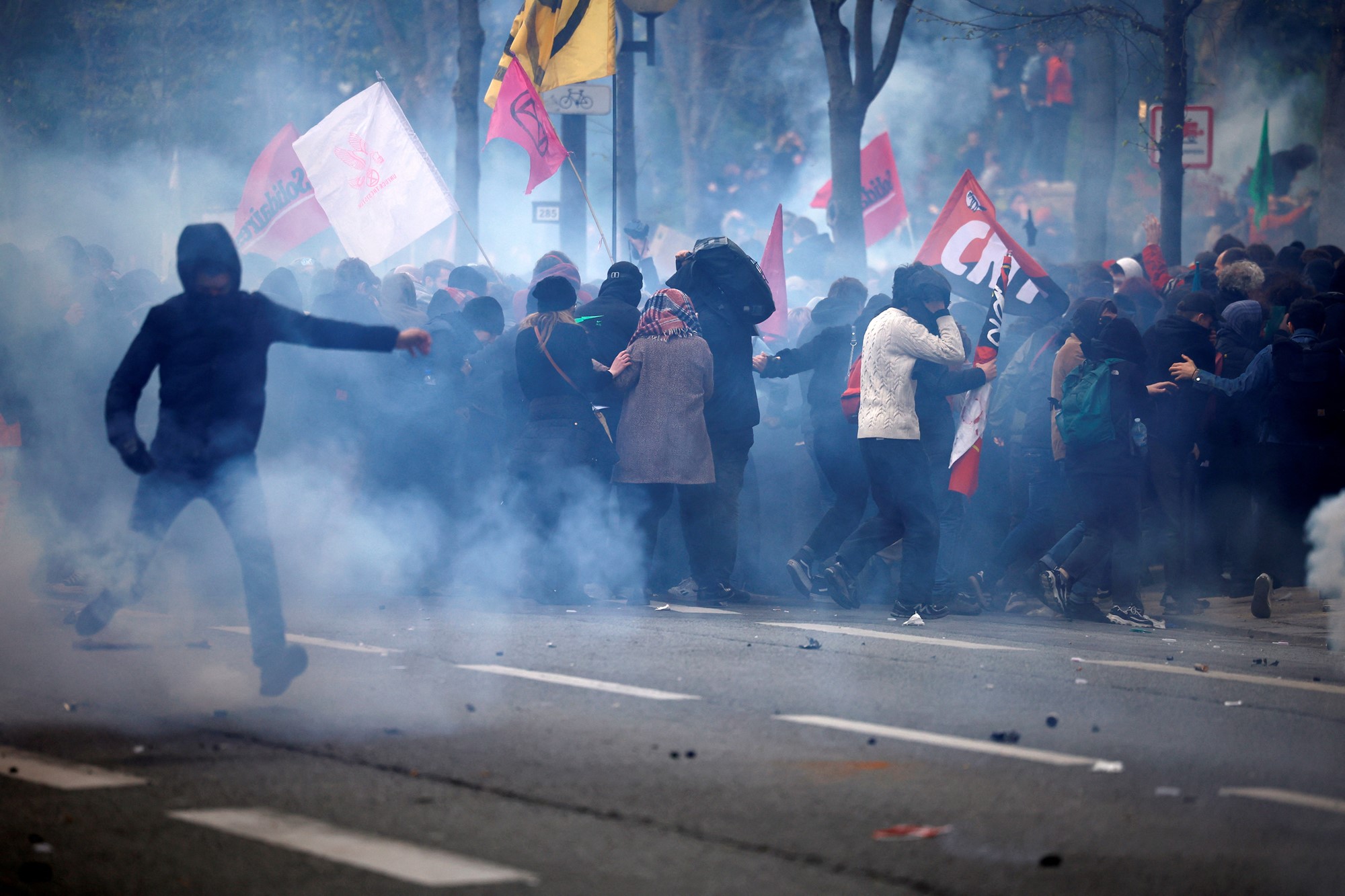 Protest crowds run front smoke on a street.