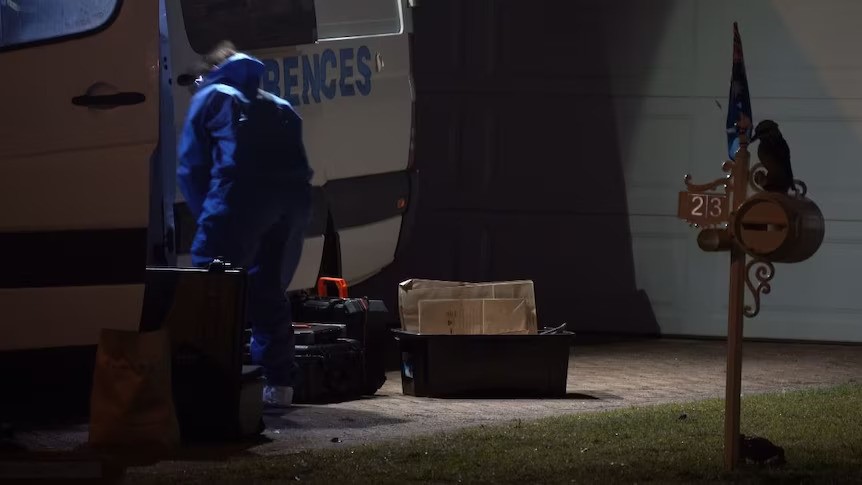 A police forensics person gets into a van in a house driveway, on which bags and documents are lying