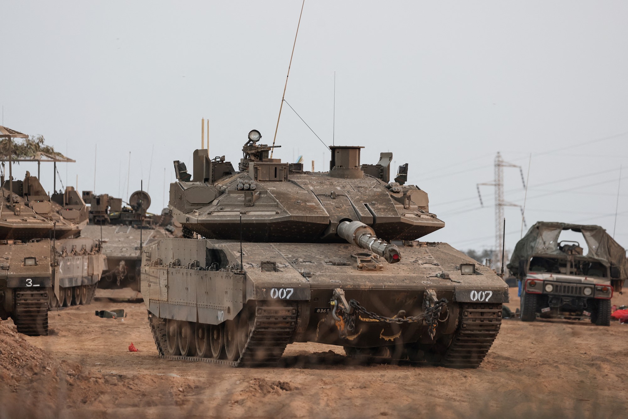 A brown tank and other military vehicles stand on some brown dirt.