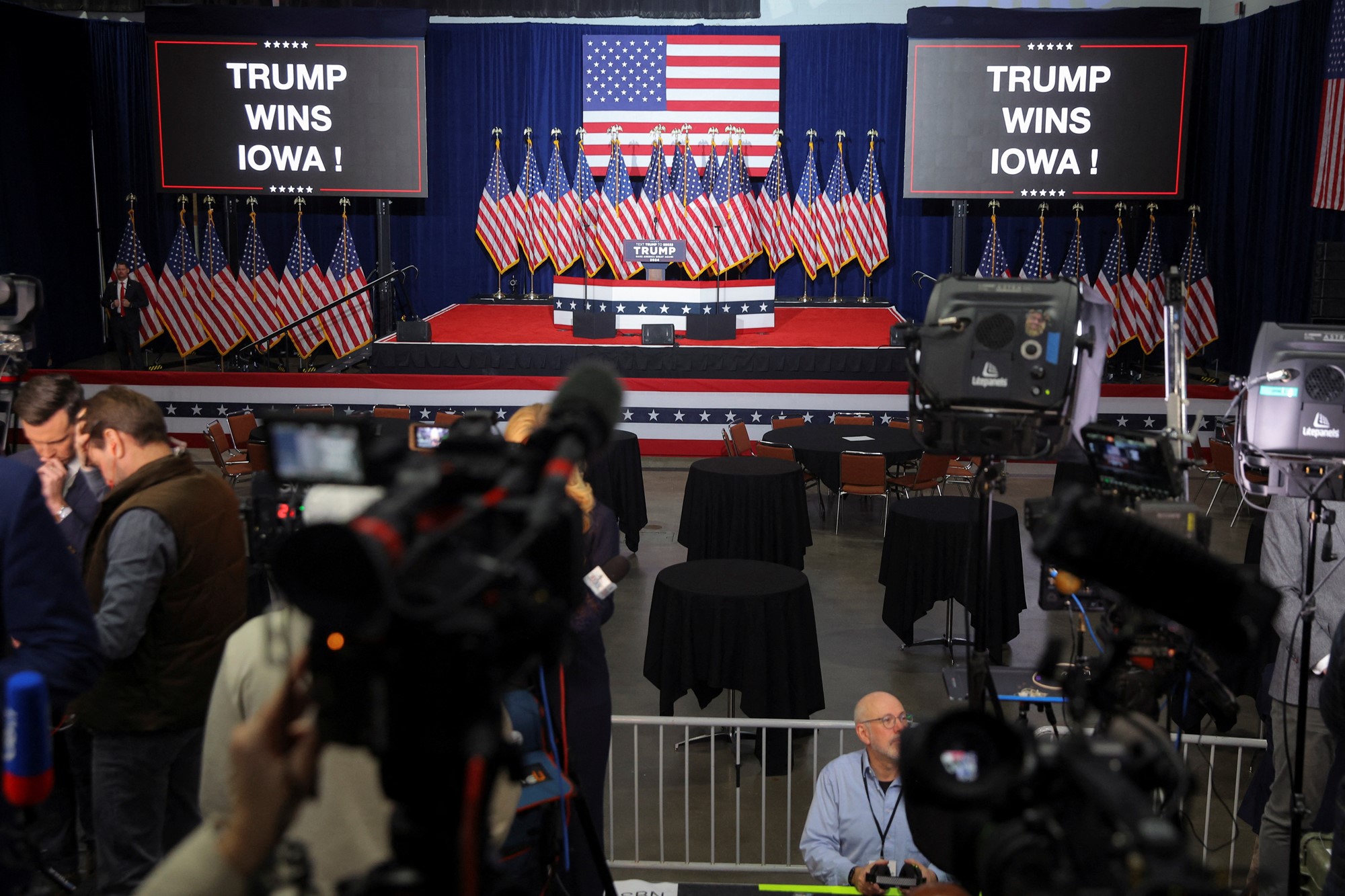 A stage set with several American flags and giant screens declaring TRUMP WINS IOWA!