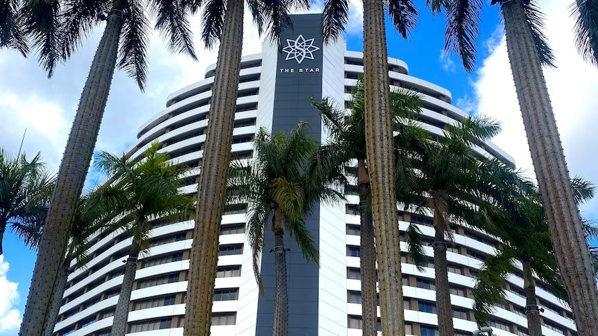 A tall casino building with the Star logo on it, behind rows of palm trees