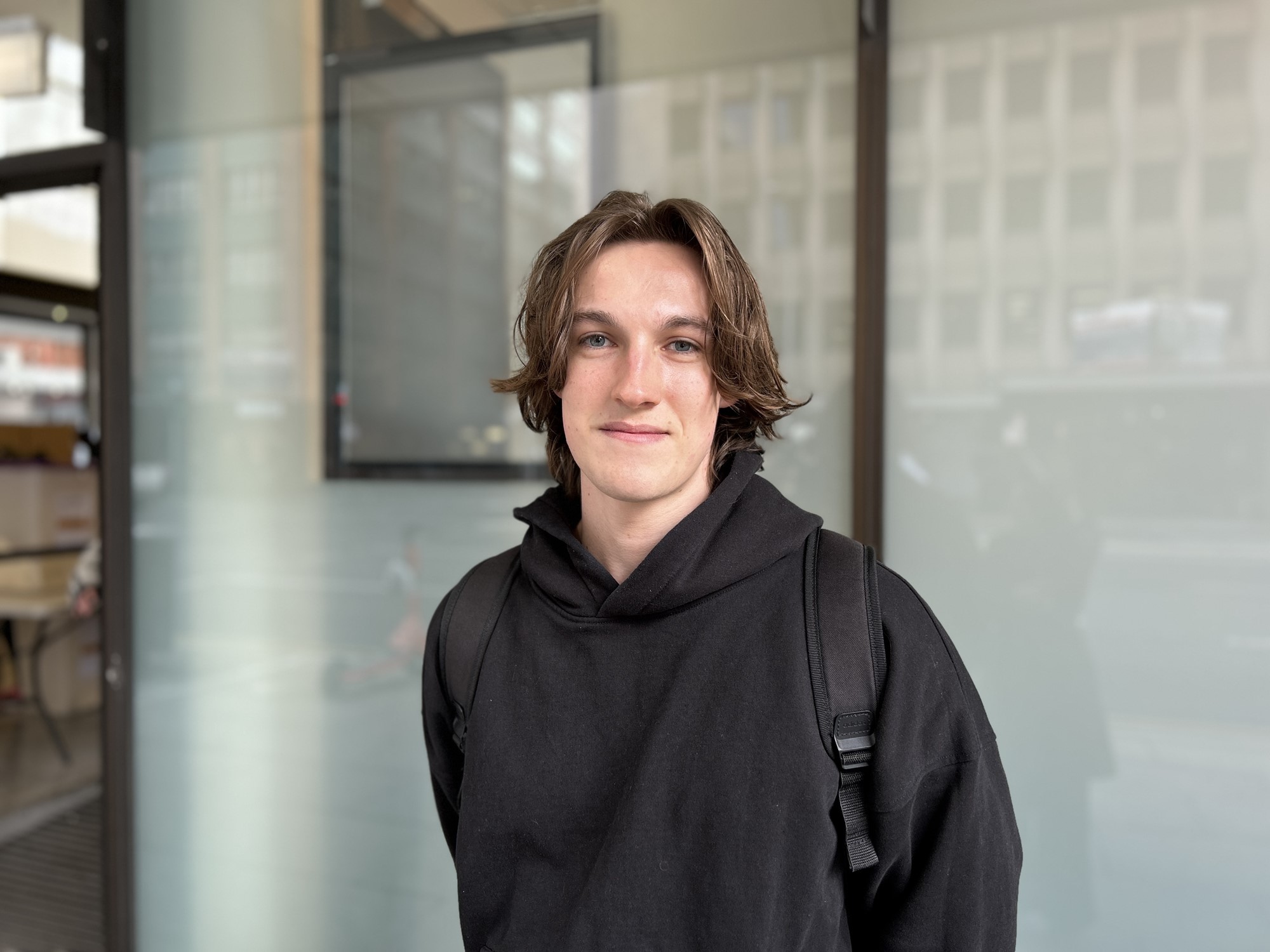 A young man in a black hoodie smiles for a photo.