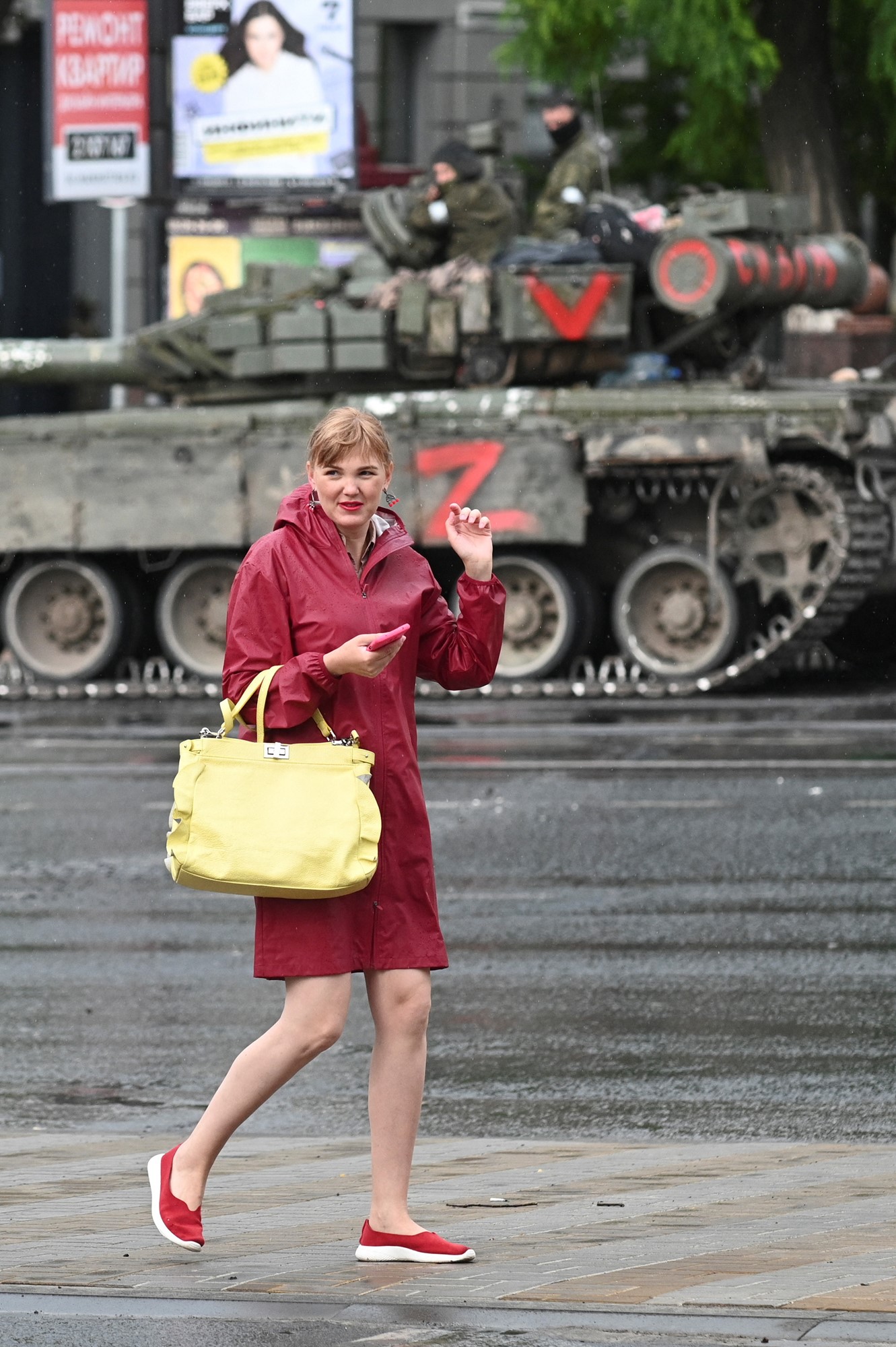 A woman in a red dress holds a large yellow handbag as she walks past a tank on the streets of Rostov-on-Don