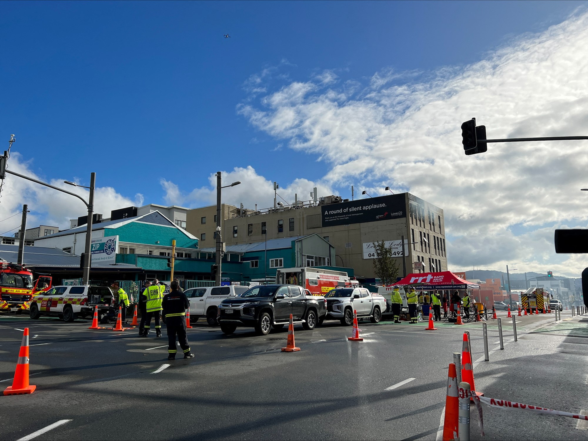 Traffic cones block a road as smokeis outside the top of a building in the distance.