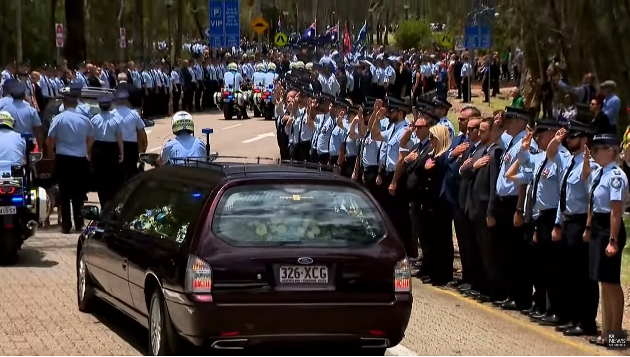 Police officers salute whil a herse drives by.