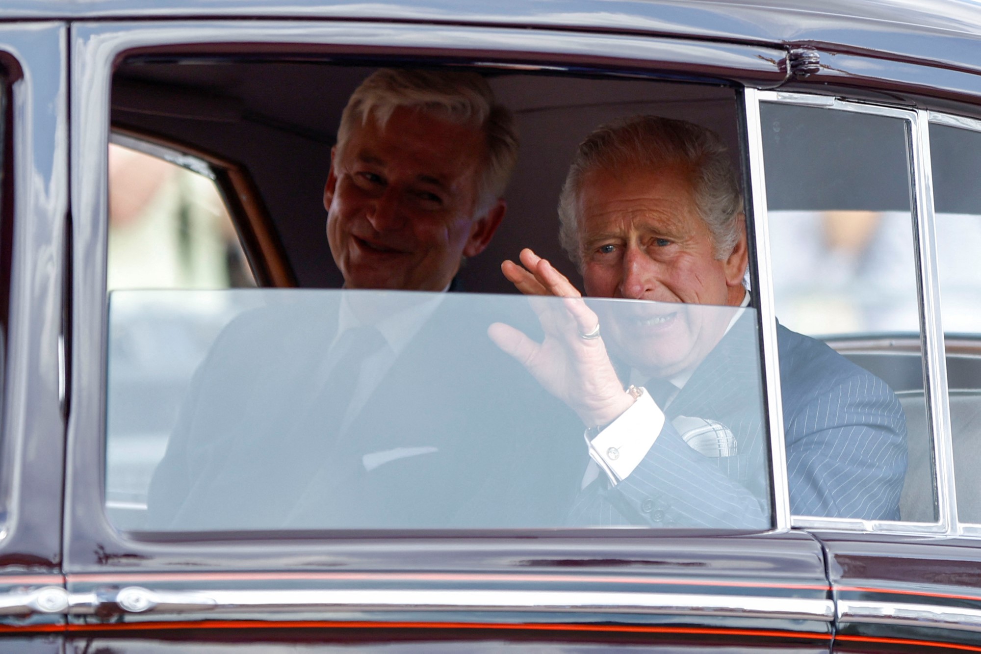 King Charles is pictured through a car window waving.