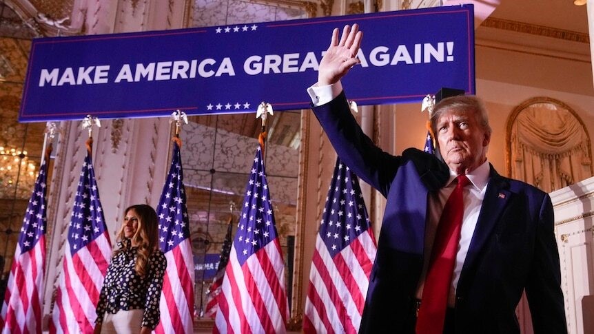Trump waves to the crowd in front of a Make American Great Again sign