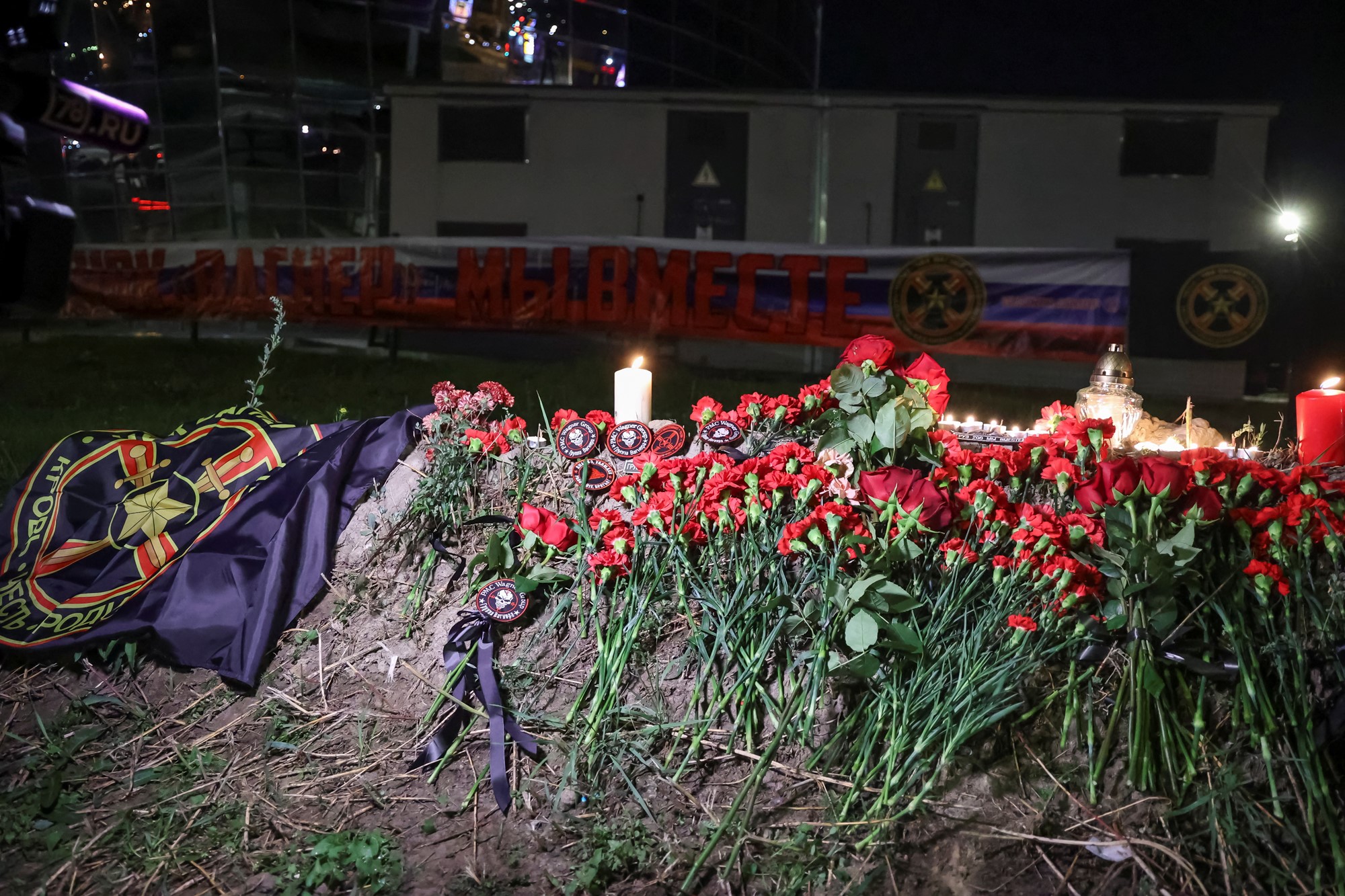 A pile of red roses, with flowers and a black flag depicting the Wagner crest