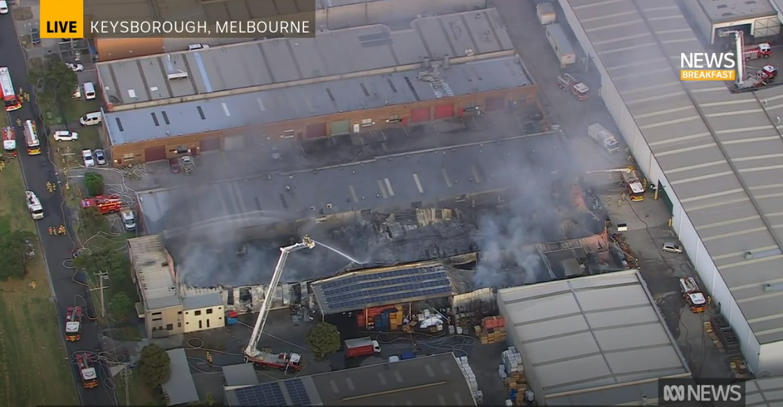 A shot from a helicopter of a large factory on fire.