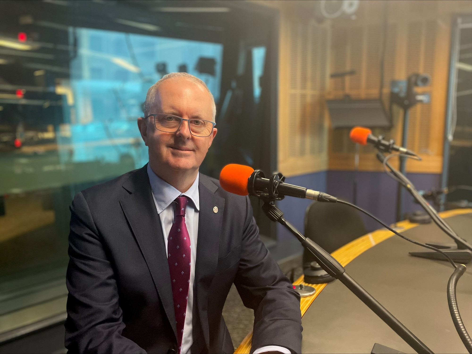 Tom sits in a radio studio and smile for a photo near a microphone.