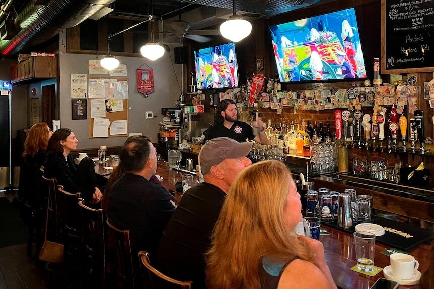 People sit on bar stools and waych the Queen's funeral on TV