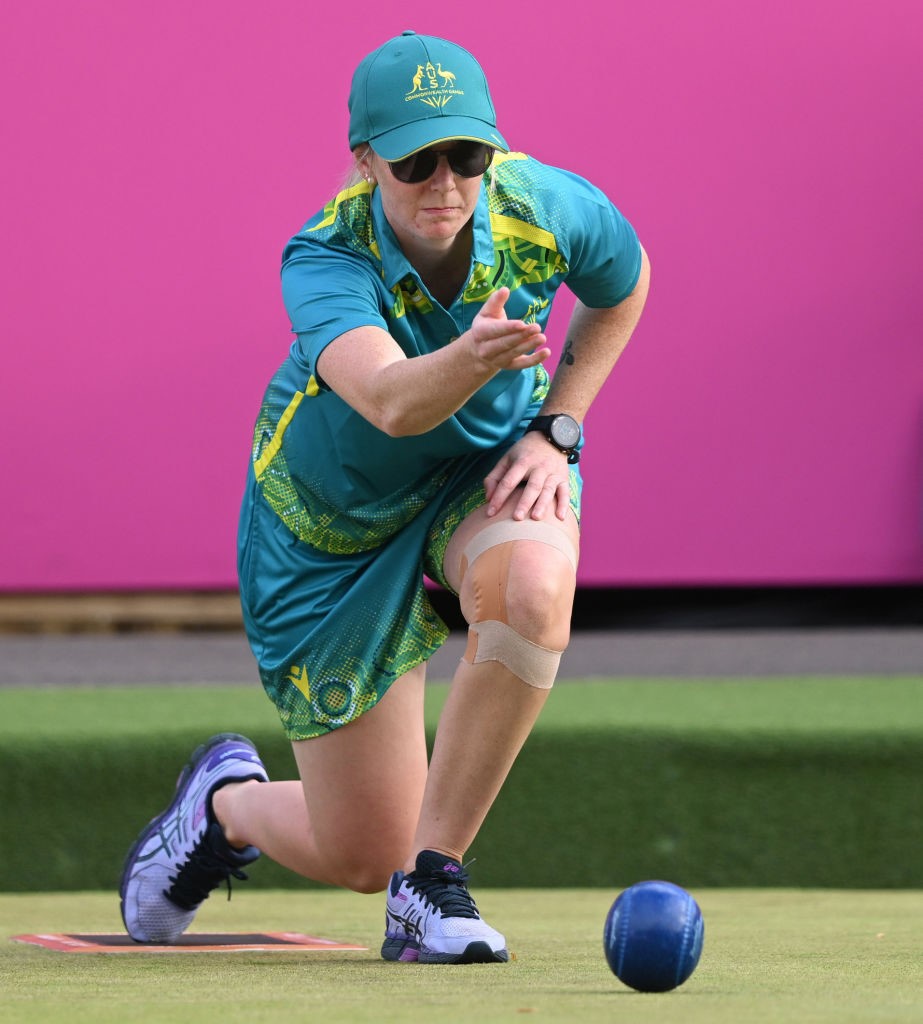 ellen ryan captured in action rolling a lawn bowls ball on a green in front of a pink background