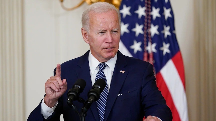 Joe Biden stands in front of microphines and holds one finger up.