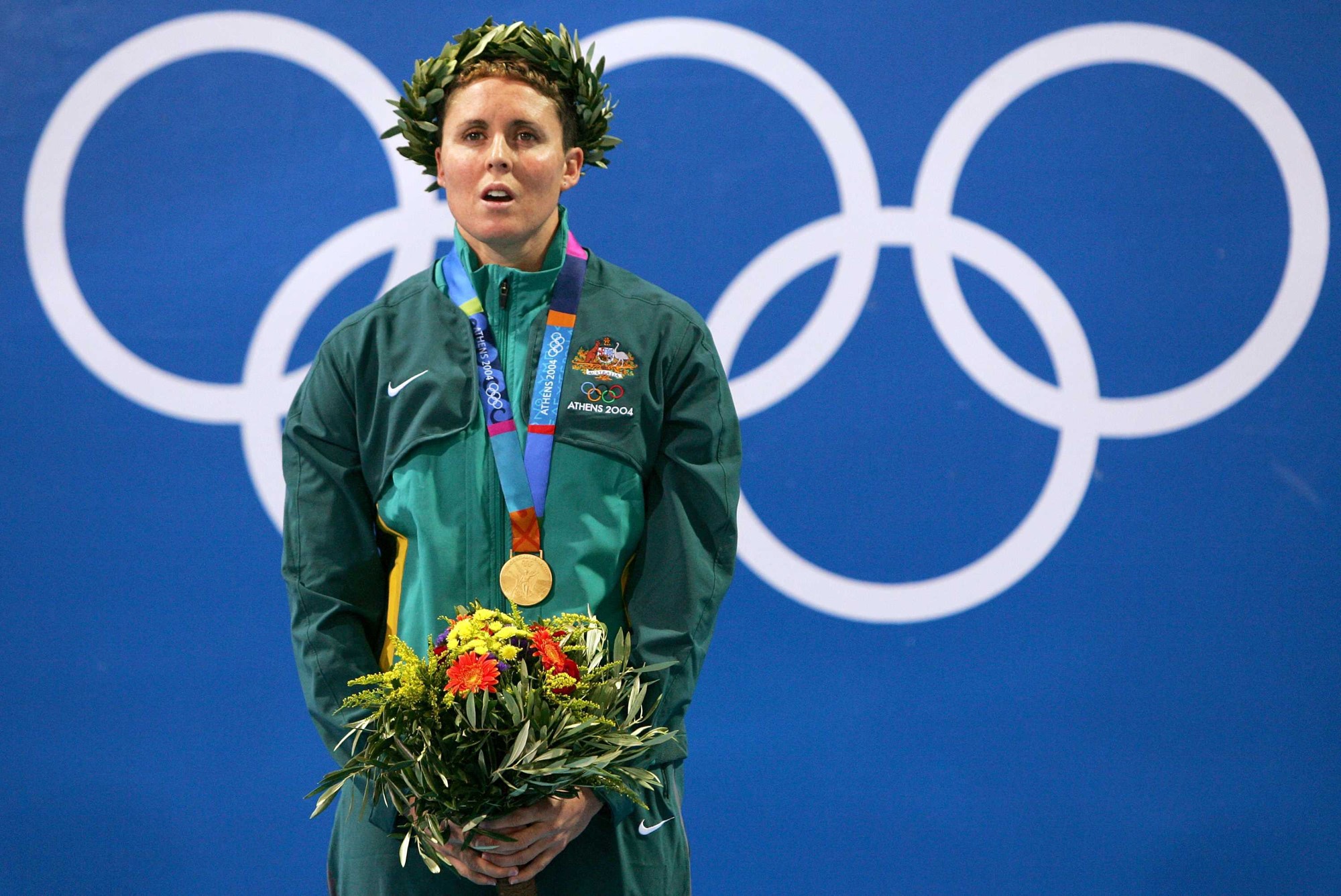 Petria Thomas with a medal around her neck, holding flowers and with a wreath on her head.