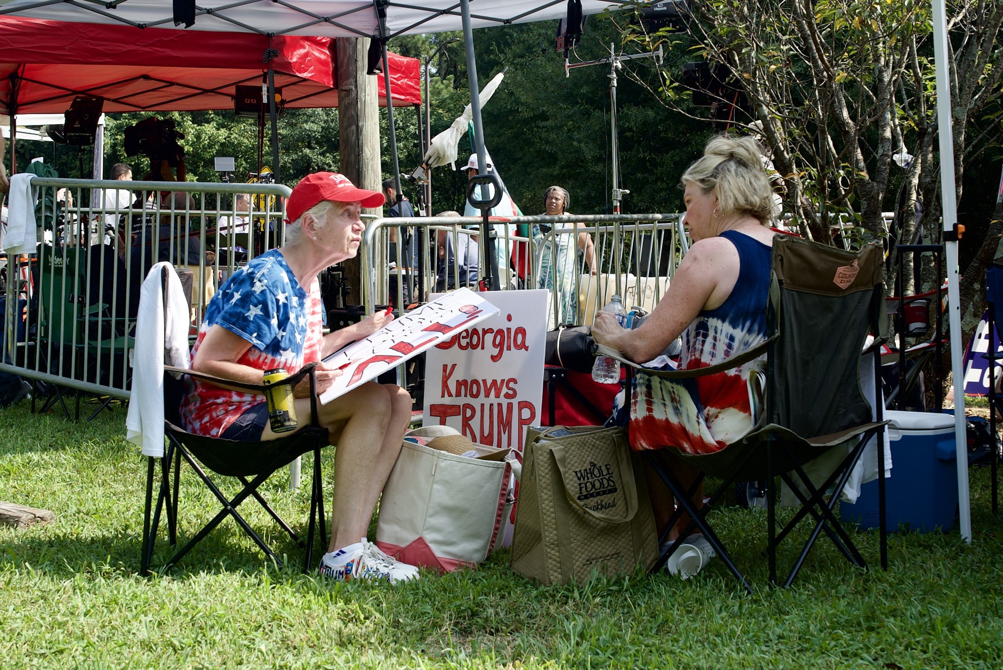 Two older women in chairs, one is colouring in letters on a handmade sign. The woman on the left with the sign is Marsha, the one on the right is Cathy