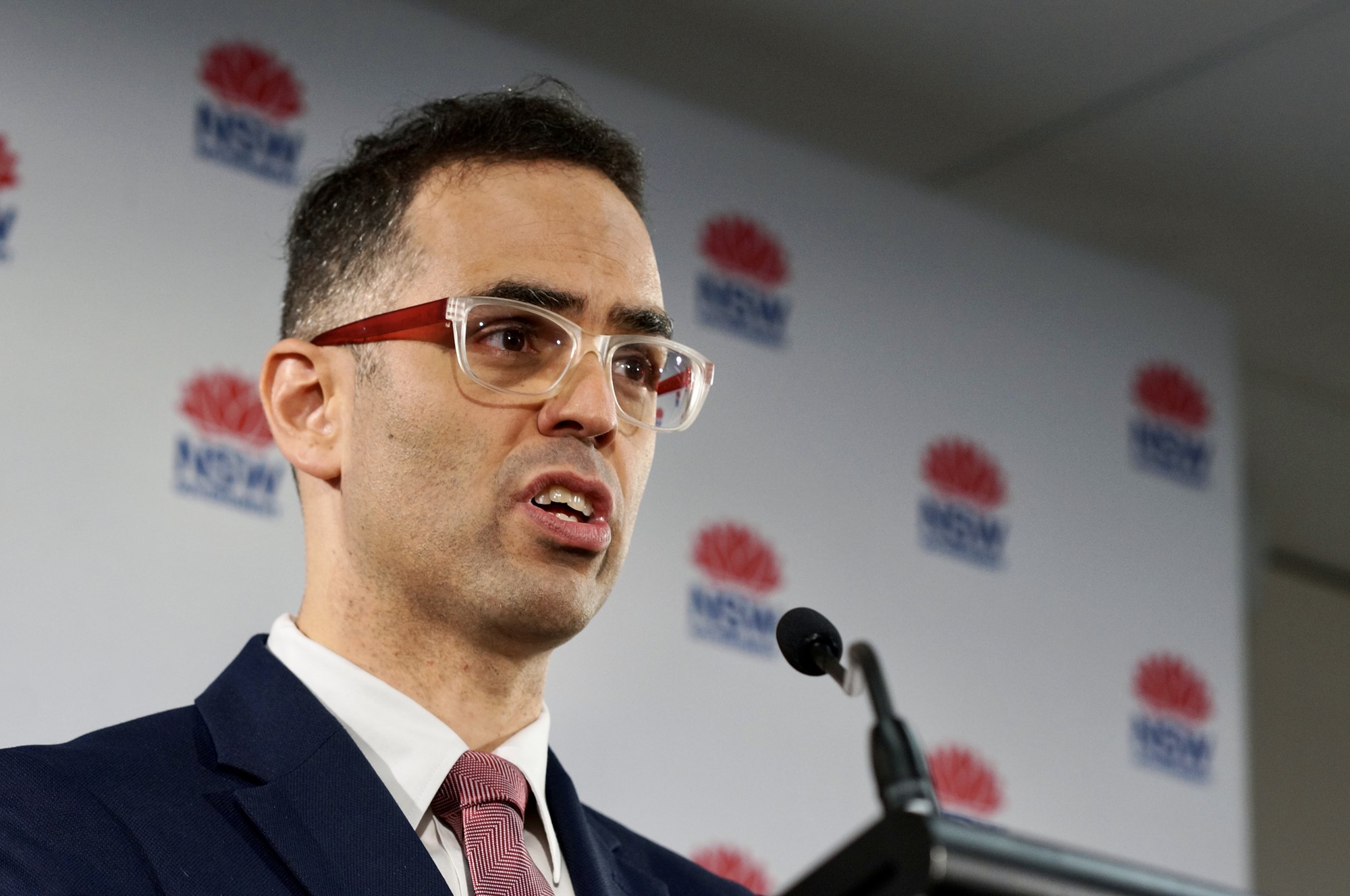 A man with glasses speaks in front of a NSW government sign