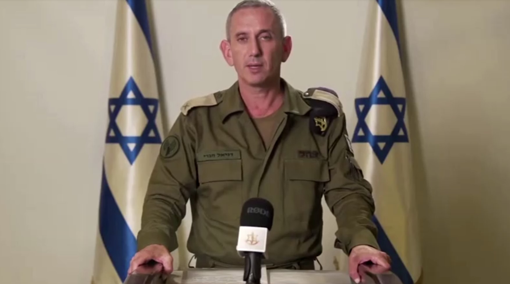 Daniel Hagari in uniform in front of two Israeli flags speaks at a microphone