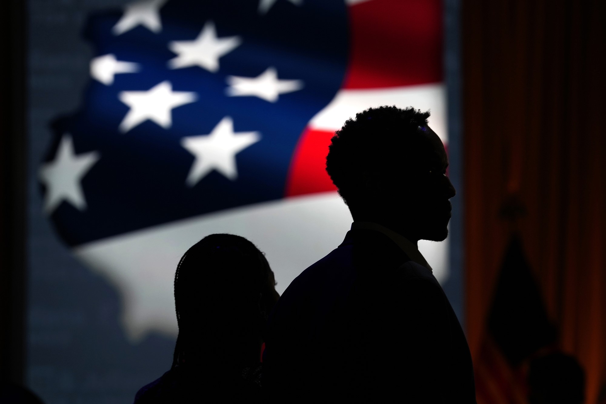 The silhouette of two people standing in front of the American flag.