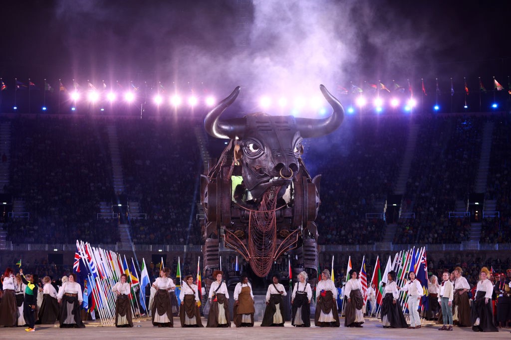 a giant 10m tall mechanical bull in the middle of a lit-up stadium with performers in front of it