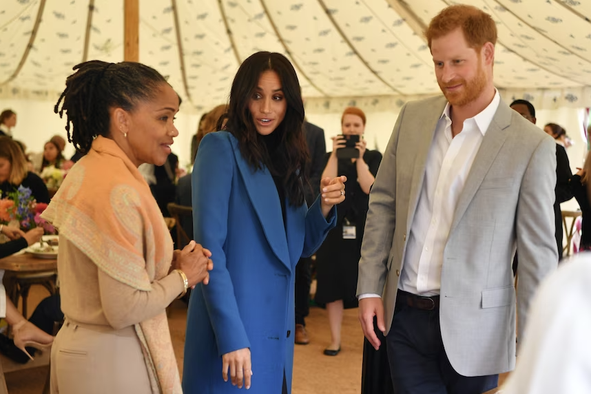 A middle-aged woman chats with Prince Harry and Meghan Markle.