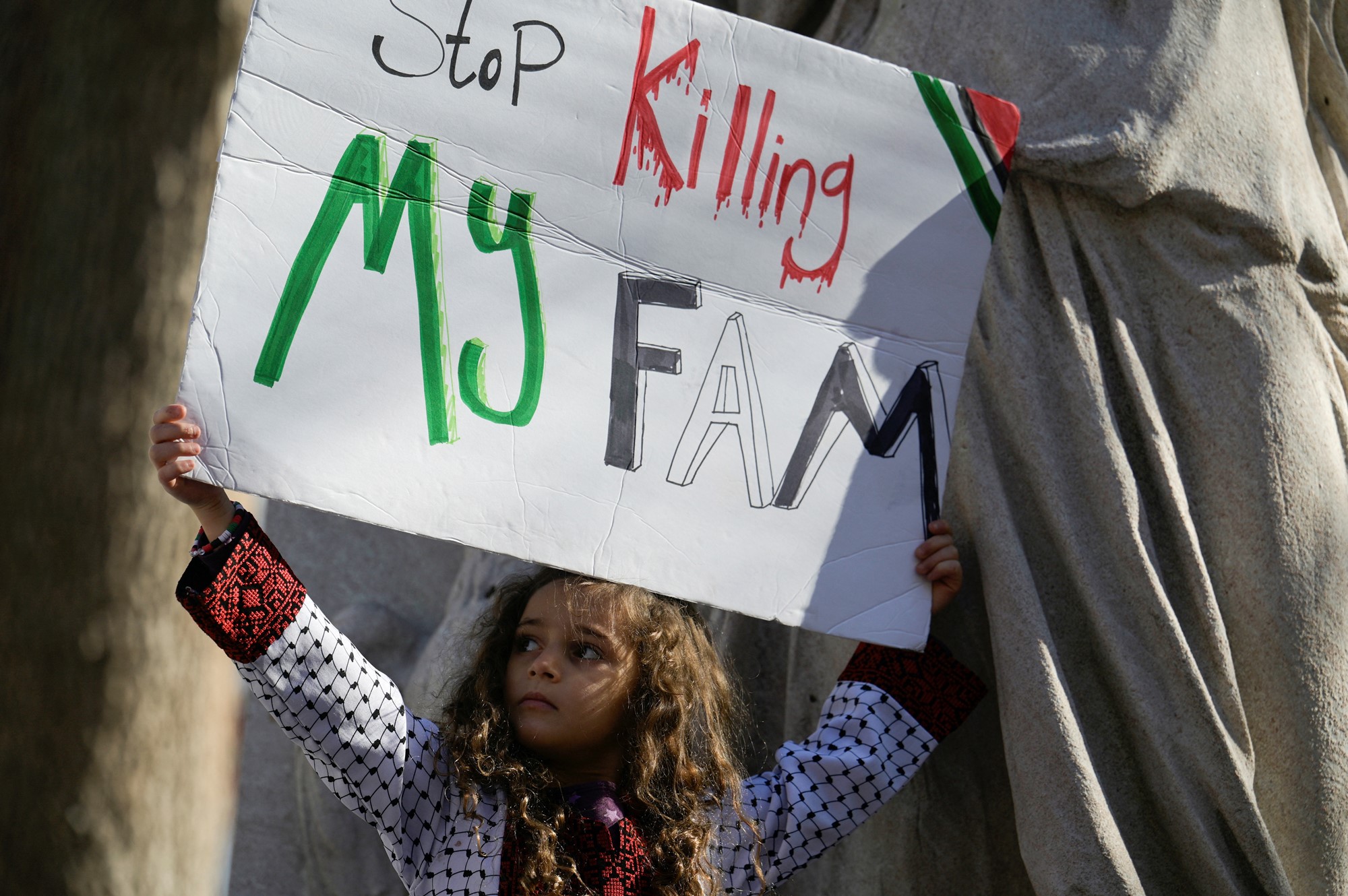 Young girl holds sign saying 'stop killing my fam'