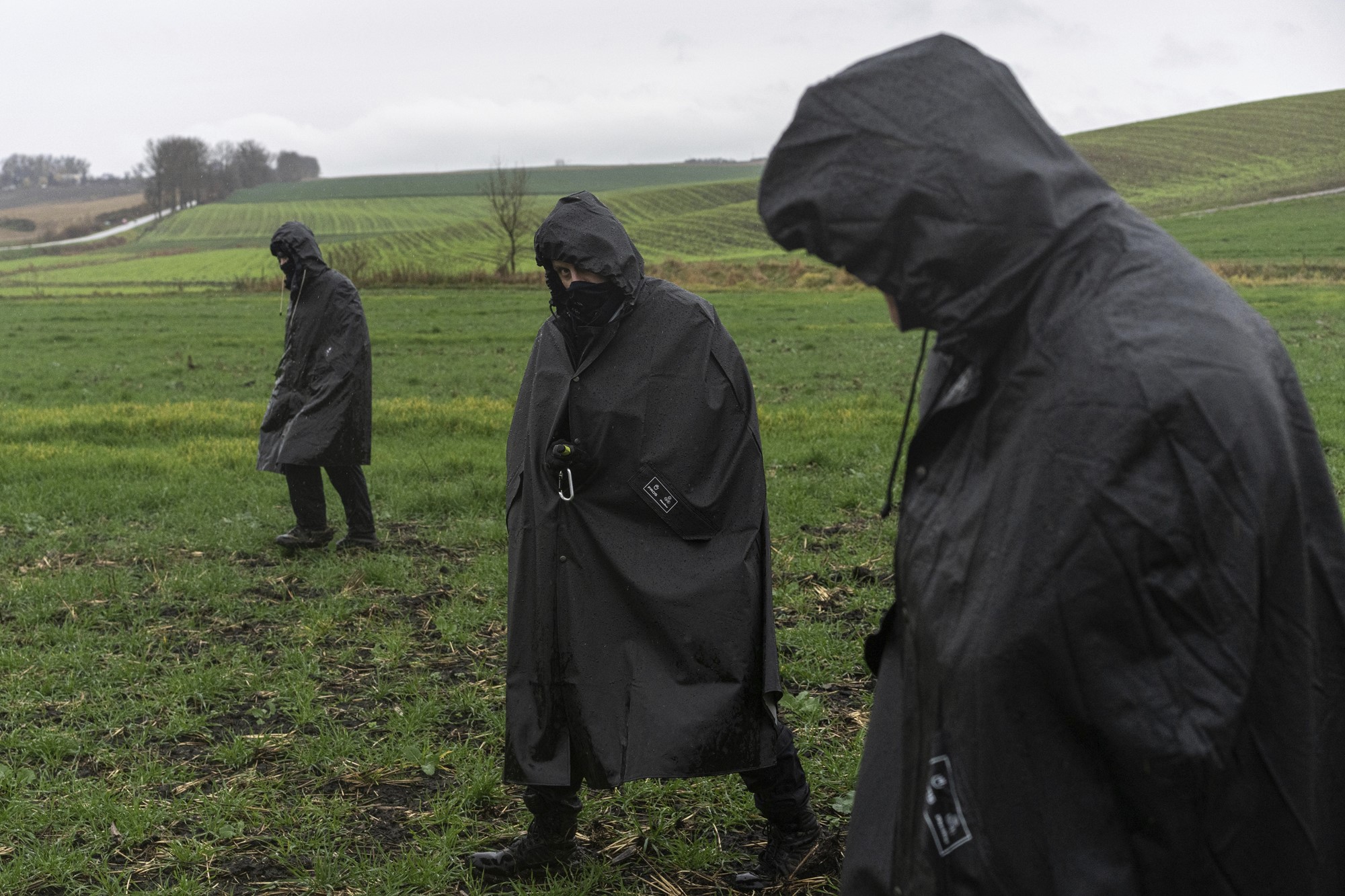 Three men in black anoraks search a wet grassy field