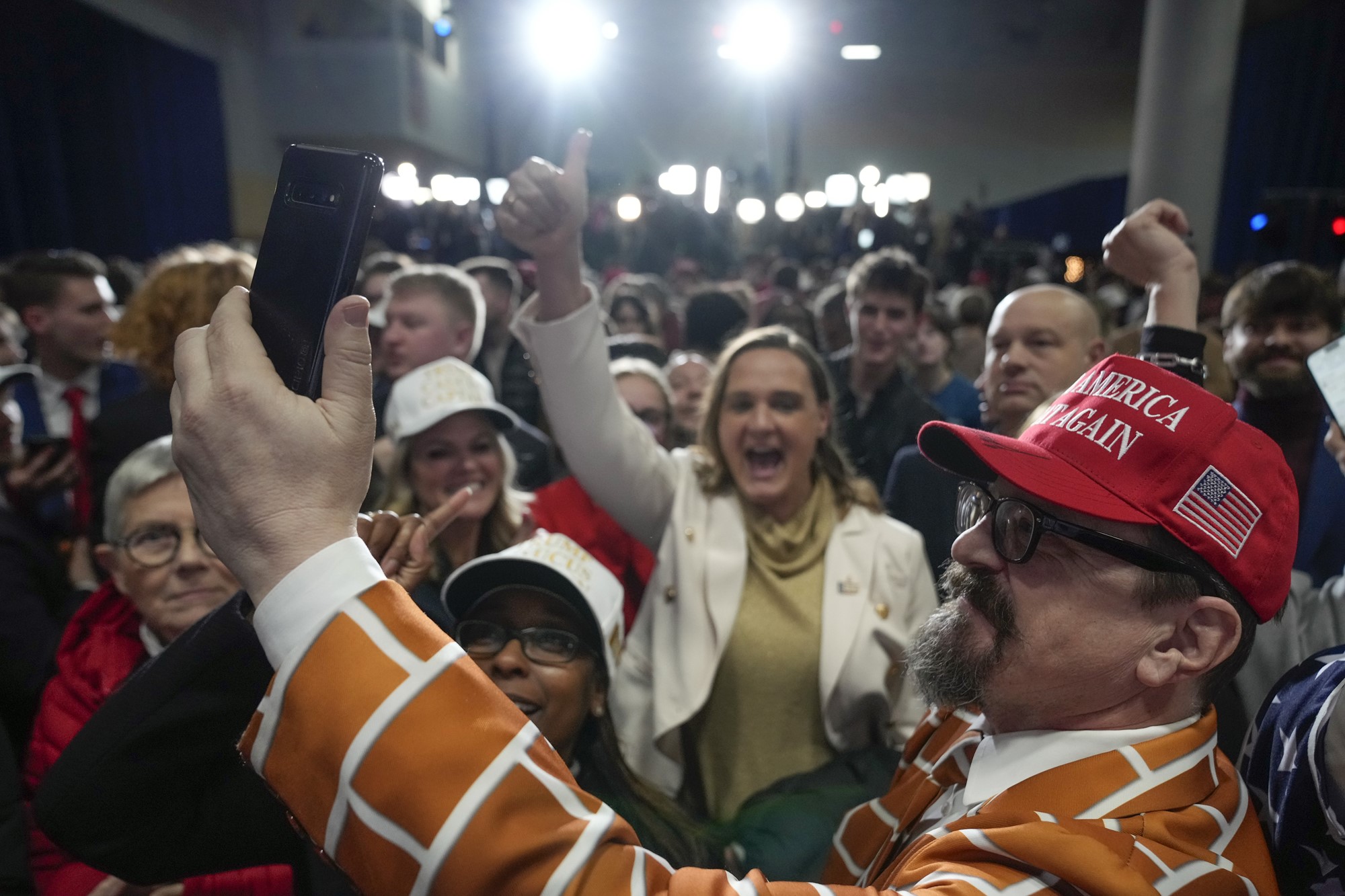 A man wearing a red Make America Great Again cap holds his phone up to take a selfie with the crowd