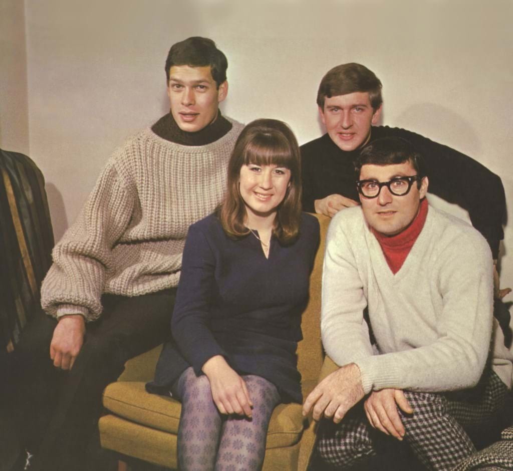 The members of The Seekers sit together on a couch.