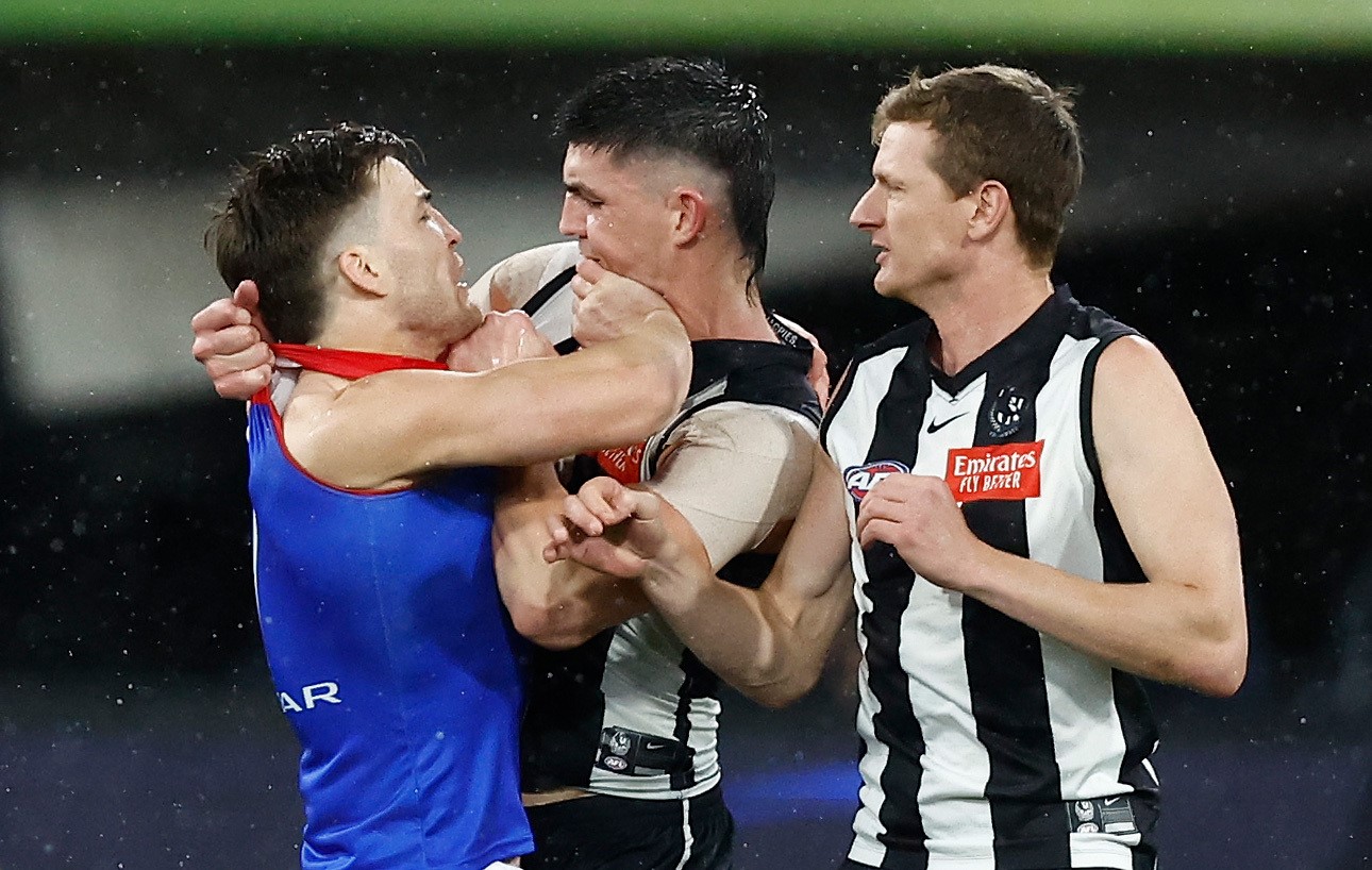 A Melbourne player and a Collingwood opponent stand toe-to-toe grabbing each other's guernseys after an incident.