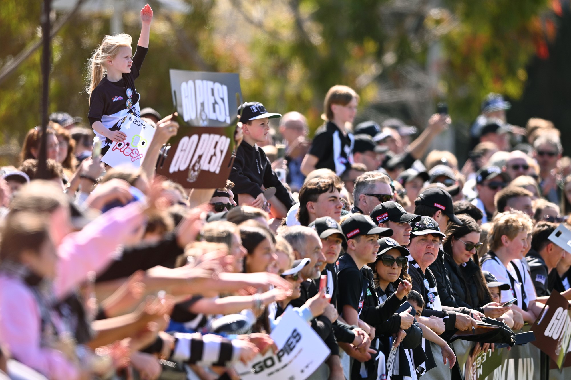 Coolingwood fans decked out in black and white with signs gather at a previous open training session.