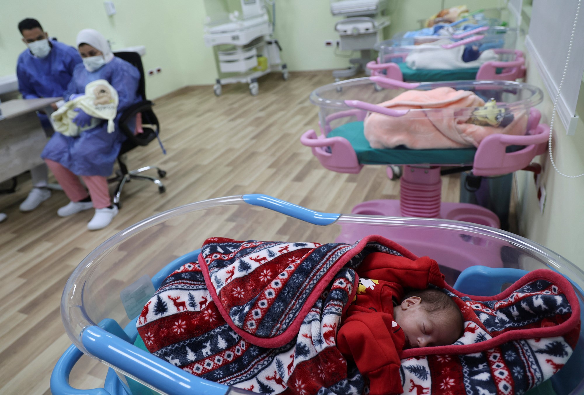 Row of babies in cribs with colourful blankets. 