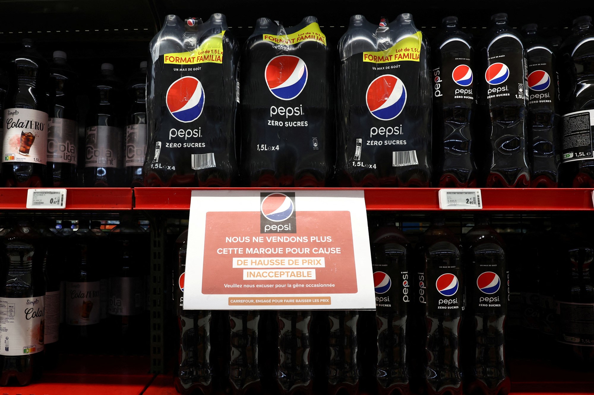 A shelf in a supermarket stocked with large bottles of Pepsi Max. A sign is fixed to the front of the shelf in French, which translates to telling customers that the products will no longer be stocked in the supermarket due to unacceptable price increases.