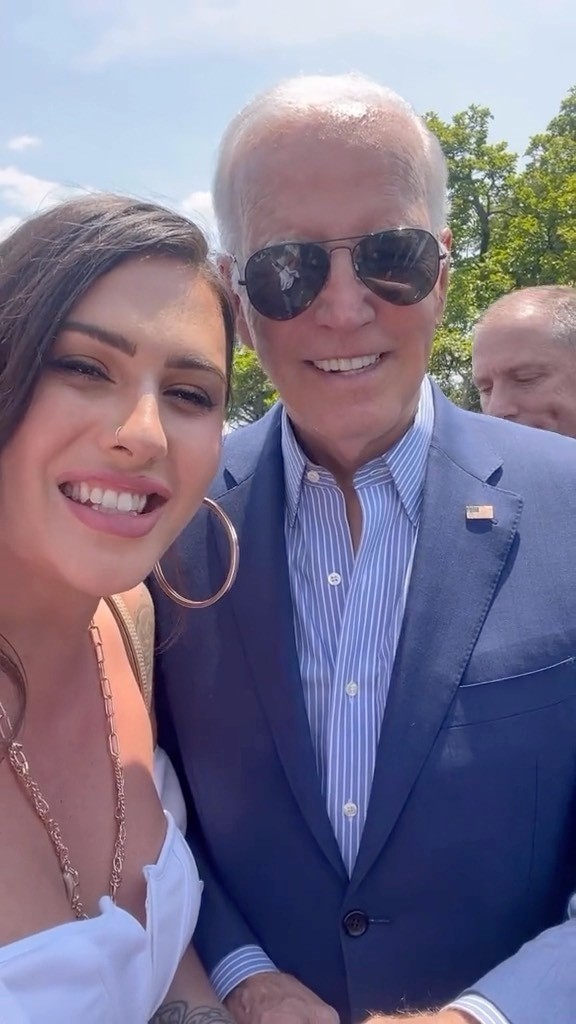 A woman smiles next to Joe Biden, who smiles and wears a suit and sunglasses