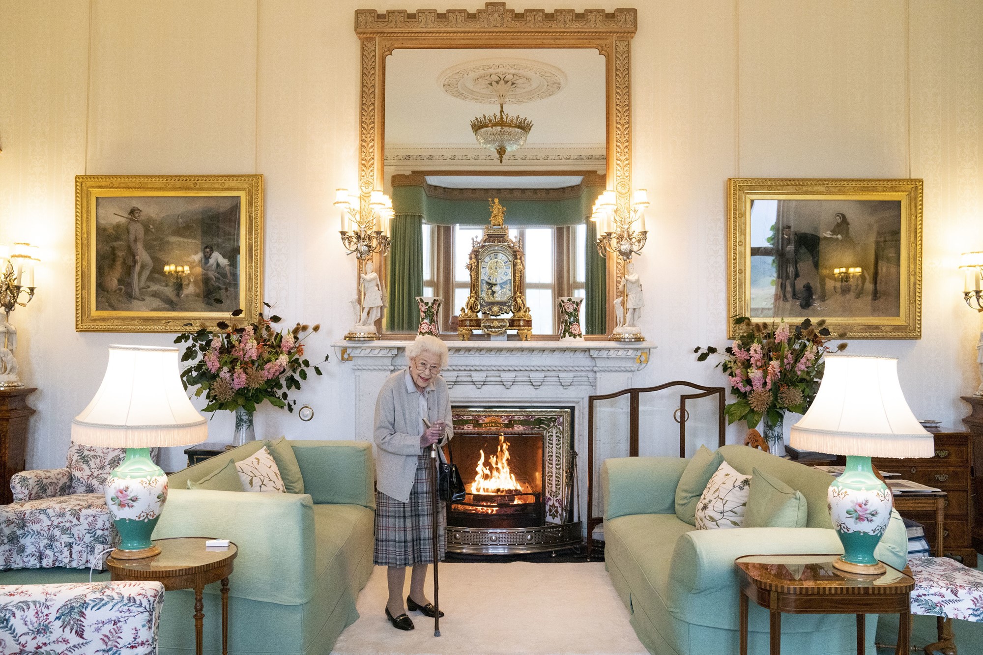 the queen stands in a sitting room beside a green couch