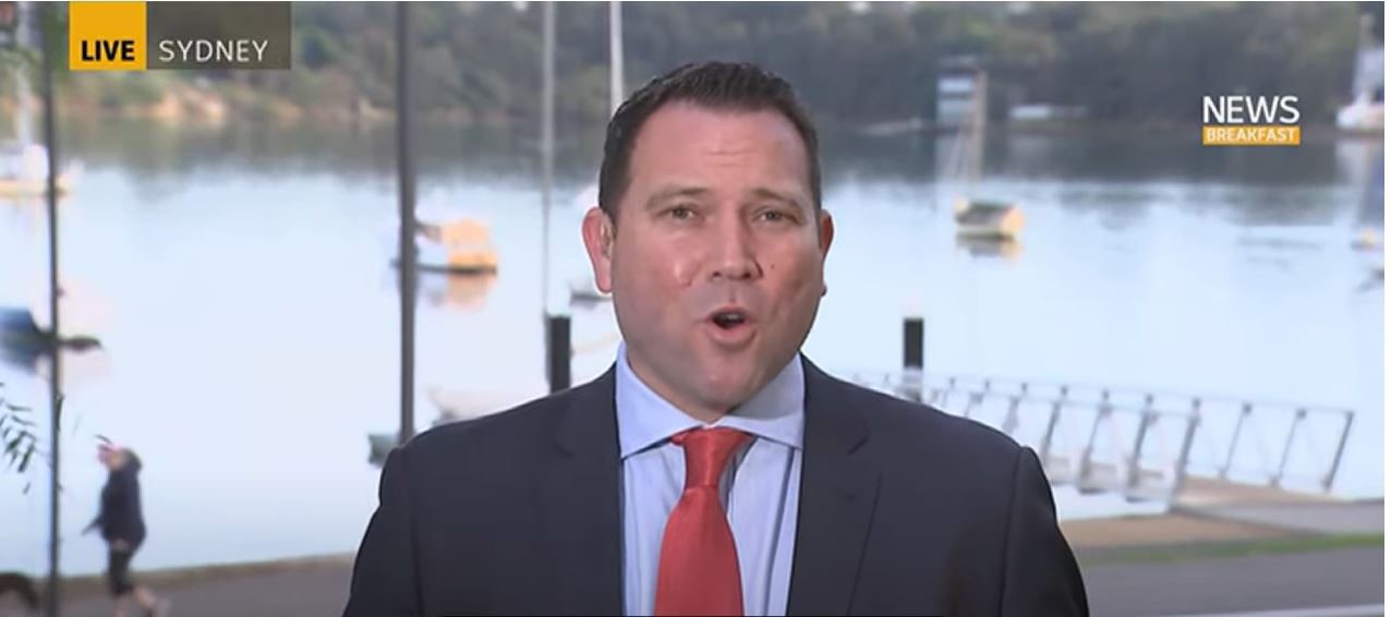 A man with cropped brown hair, red tie and black suit speaks to abc breakfast