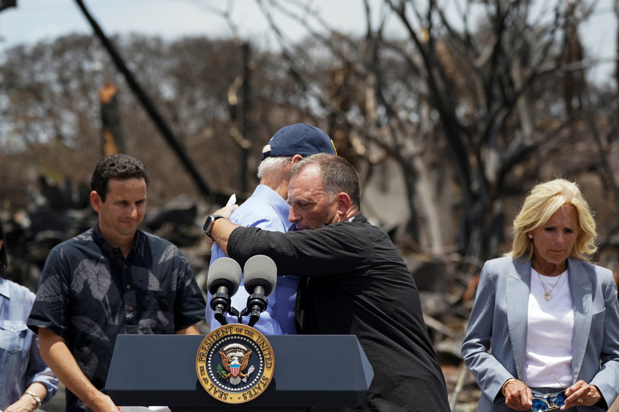 Biden hugs leaders at the podium giving a speech