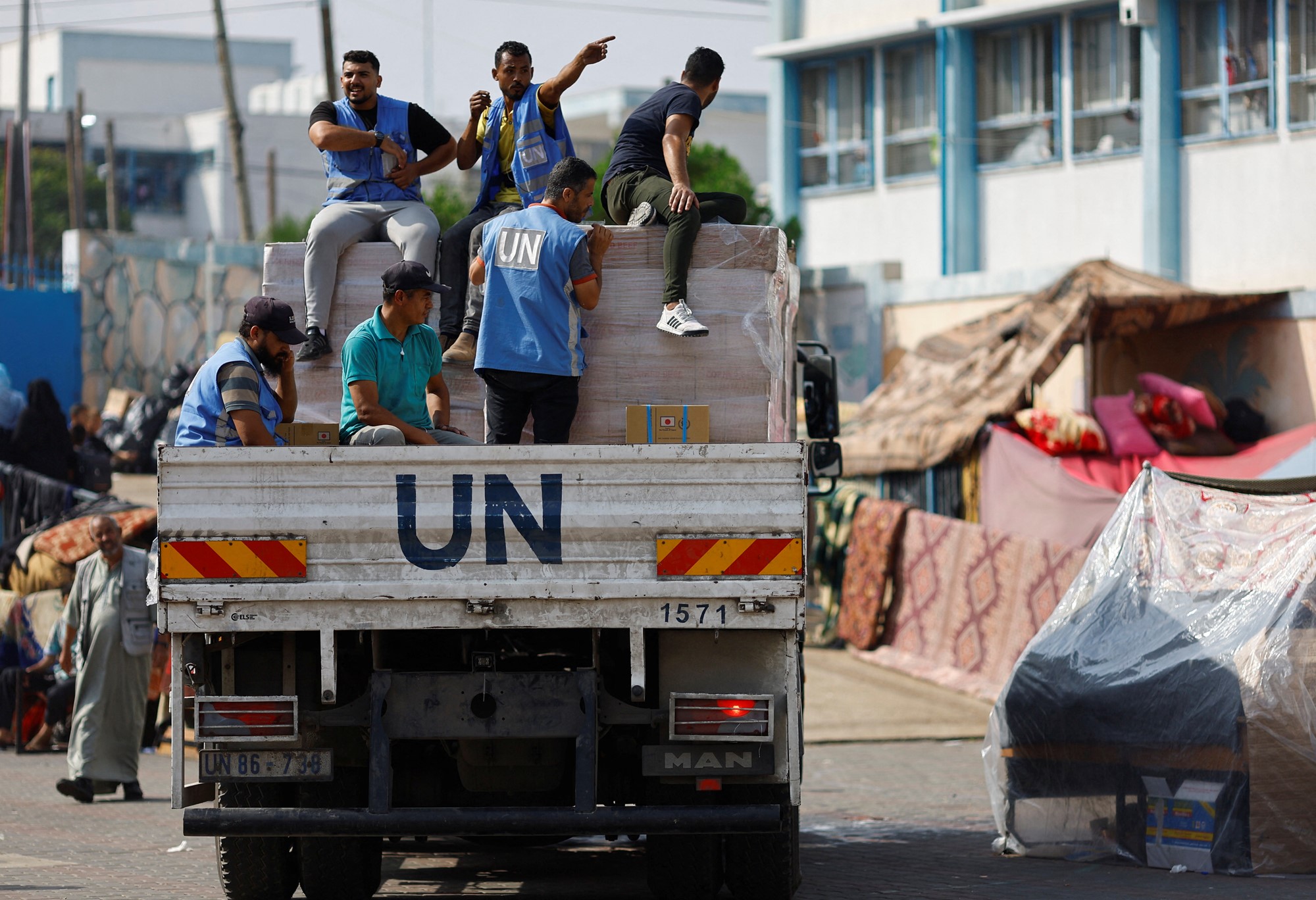 Men wearing UN-branded vests ride at the back of a truck