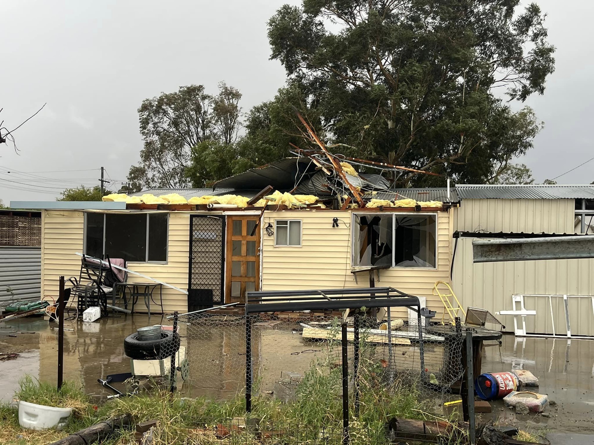 Flood waters surround a house with shattered windows and debrief on its roof.