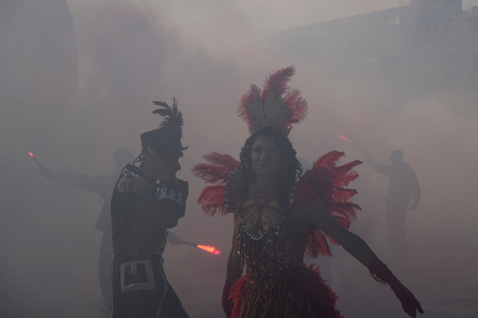 A man and woman wearing carnival costumes  dance amid smoke.