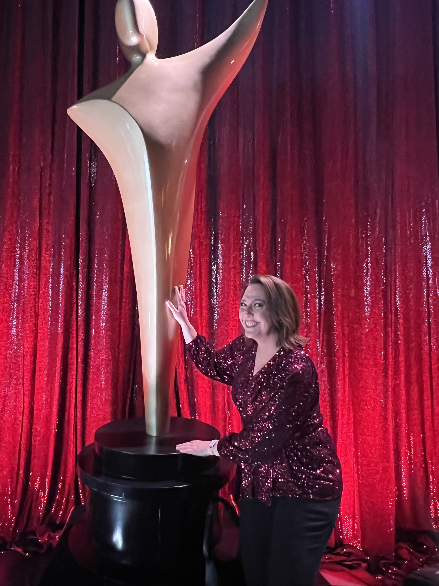 Lisa smiles next to a huge AACTA trophy statue.