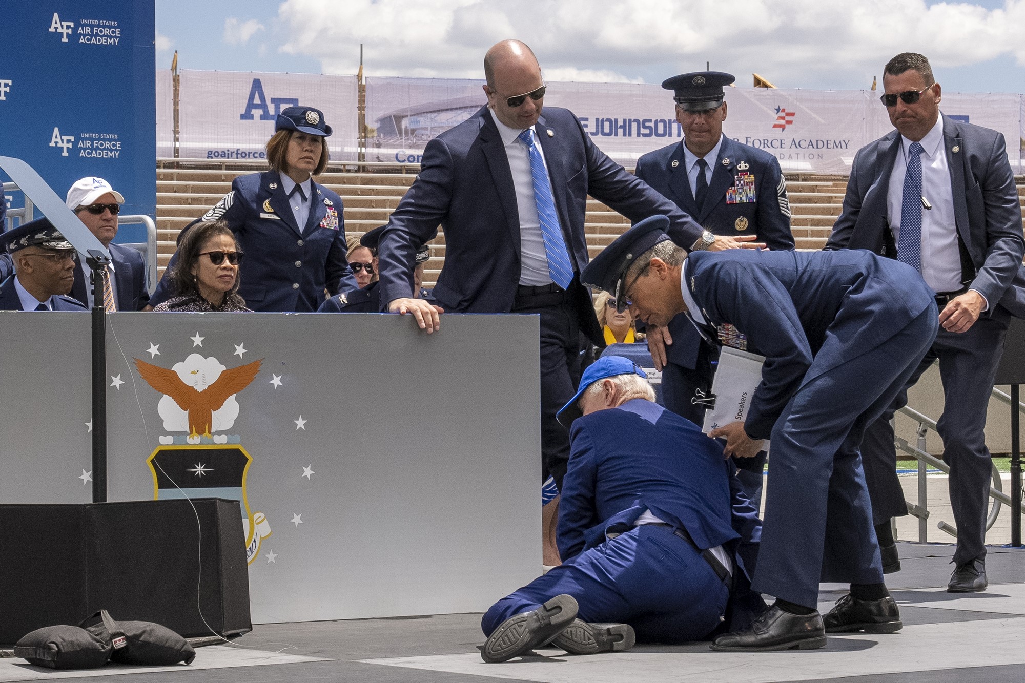 Joe Biden lies slightly on the ground of a stage, as officials crowd around him