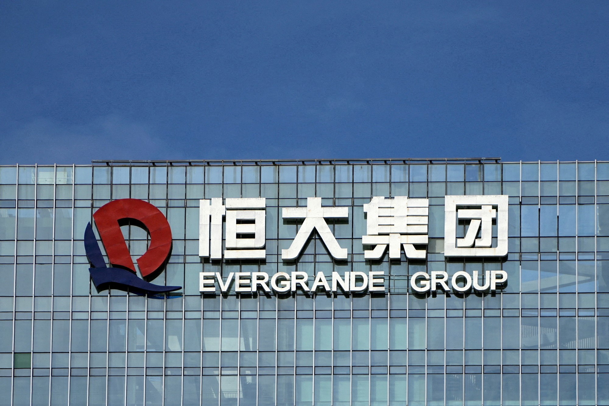 A company logo that reads 'Evergrande Group' with Chinese characters above it, suspended on the side of a large glass office building.
