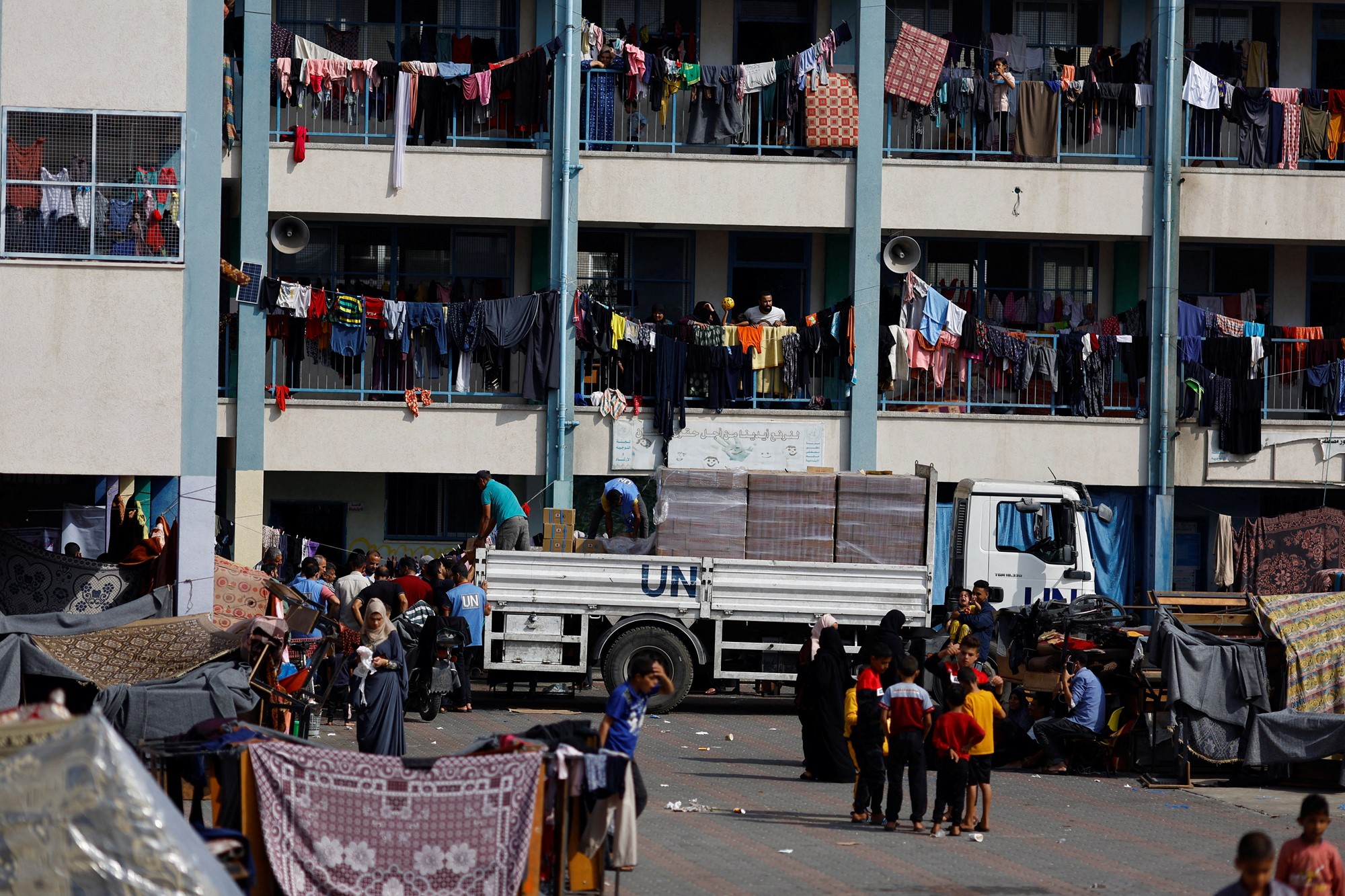 Men hand out aid off of a UN-branded truck as people watch on from balconies.