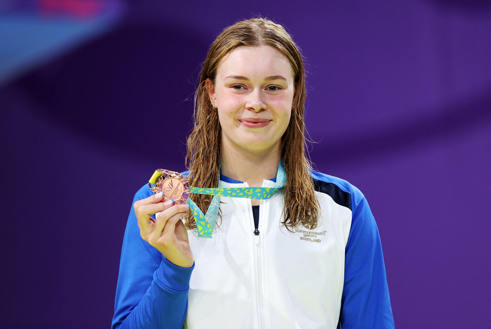 swimmer katie shanahan holds up a bronze medal, her nails match her sporting kit