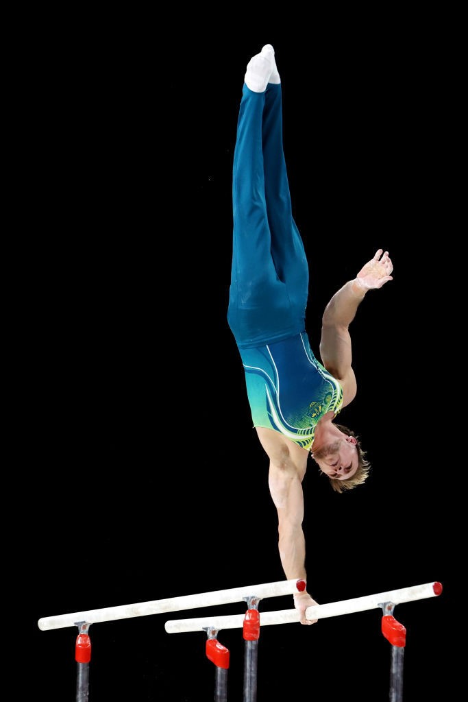 A man holds himself upside down with one hand on the parallel bars